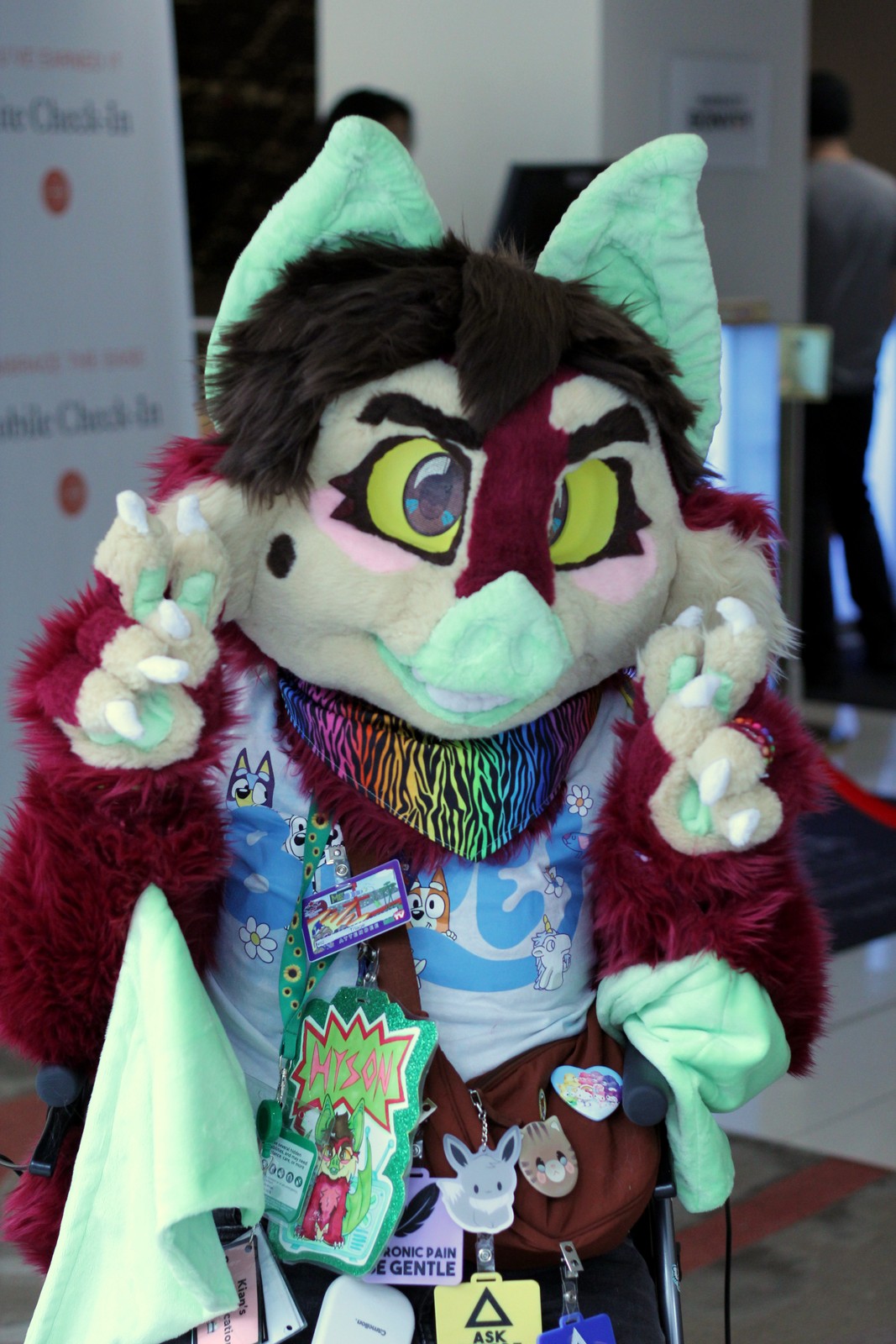 Bat fursuiter with red, pink and tan fur, green skin and brown hair making peace signs with his fingers